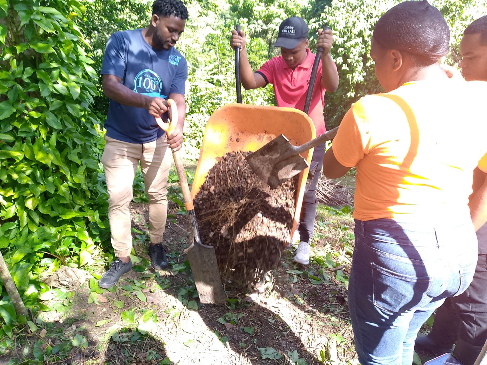 Grupo de personas trasladando compost en una carretilla.